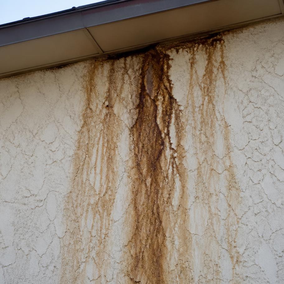 Brown water staining running down a stucco wall under an eave